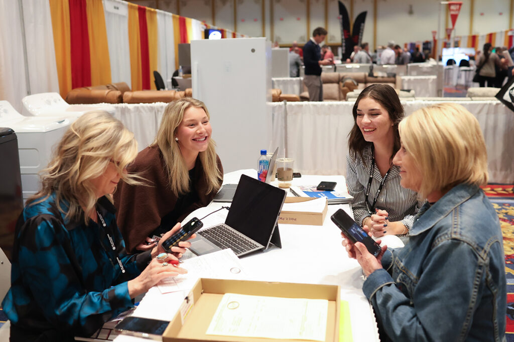 Four women seated at a table in the exhibit hall reviewing products and placing an order during TRIB Meeting of the Minds.