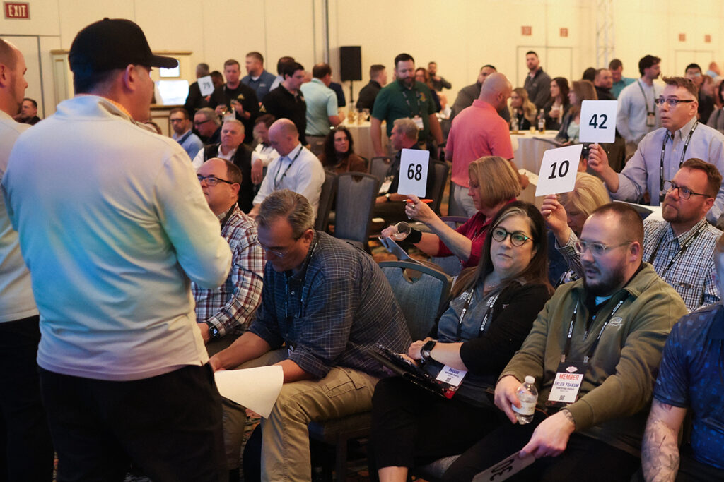 Attendees raising paddles to place orders during the high-energy HOT Show at TRIB Meeting of the Minds.