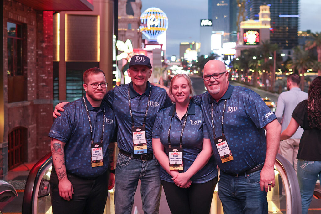 Brian Hoeppner, Thomas Roupe, Diana Christiansen, and Nick Regier from Continental Rental wearing TRIB shirts on an escalator at Ole Red Las Vegas with Paris Las Vegas in the background.