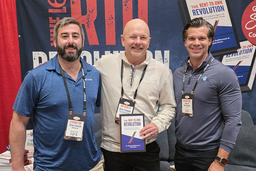 Dan Fisher posing with a signed copy of The Rent-to-Own Revolution alongside Ryan Krass and Charles Smitherman at the APRO booth.