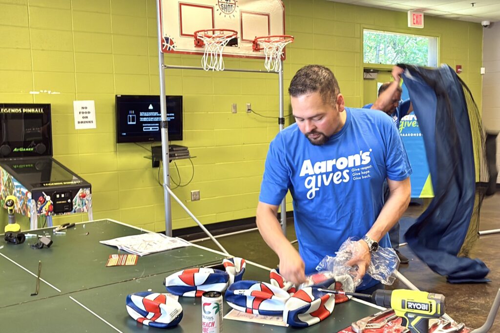 An Aaron’s associate concentrates on his tools as he assembles part of an arcade-style basketball game, which can be seen behind him.