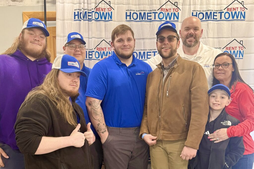 A group of Hometown RTO staffers smile as they stand around J.P. Bryant wearing a Hometown hat.