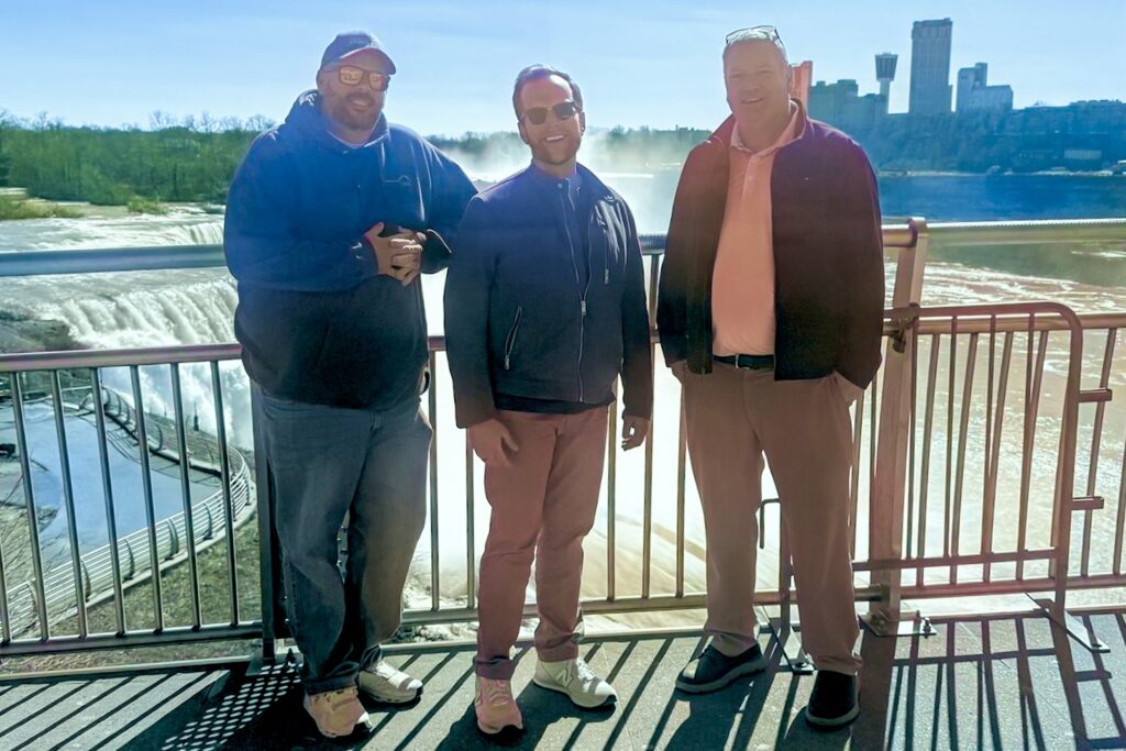 Matt Radecki, J.P. Bryant, and Jeff Smith stand in front of Niagara Falls, surrounded by heavy mist.