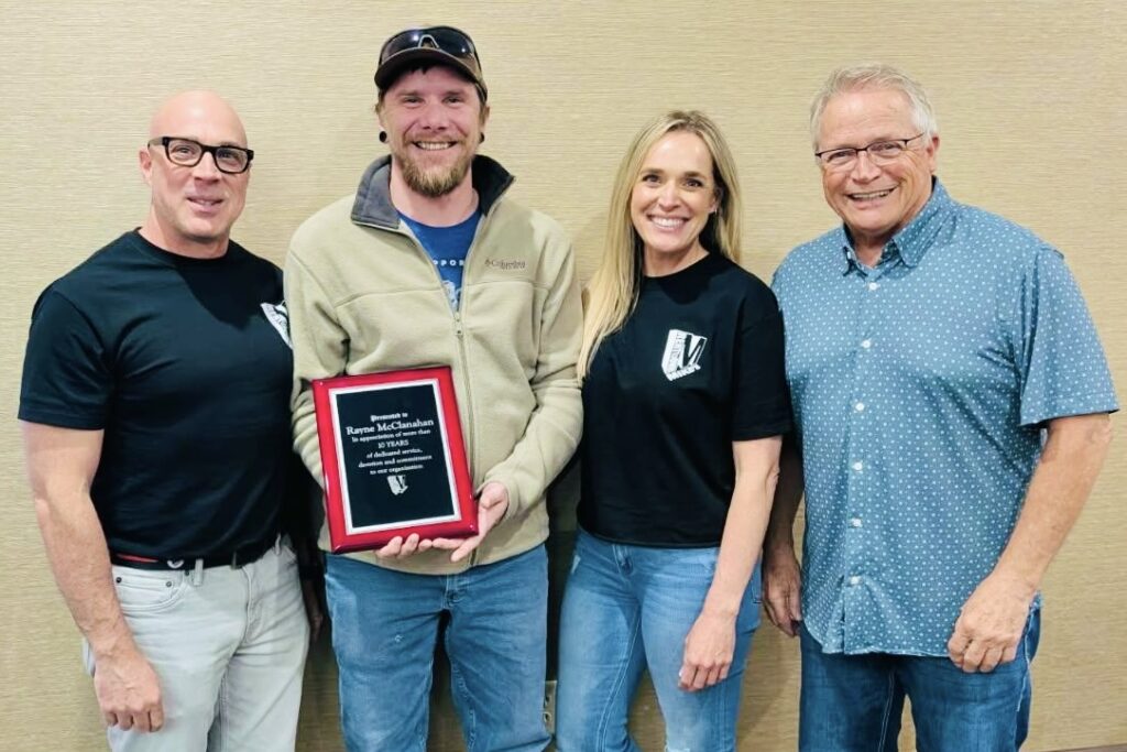 Rayne McClanahan holds a recognition plaque and smiles along with three Strong family members standing on either side of him. 