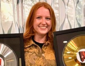 Bethany Smith holds a gold plaque in one hand and a silver plaque in the other as she smiles.