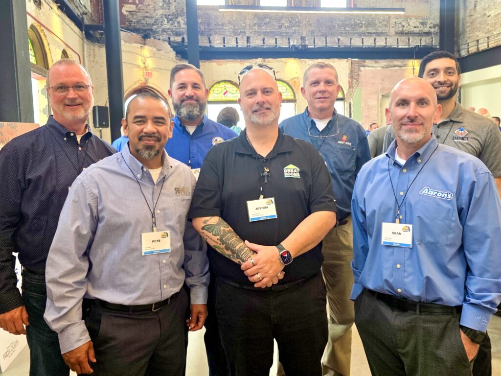 Seven men from different rent-to-own companies stand and smile.