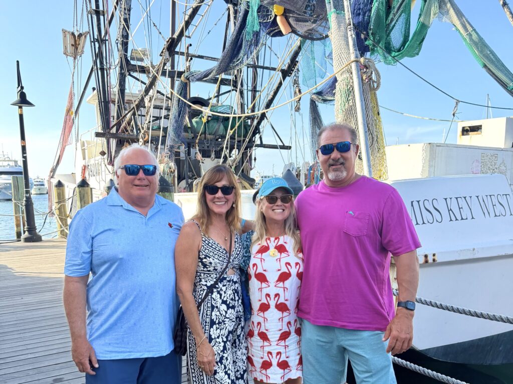 Two couples stand together and smile before a boat named the “Miss Key West.”