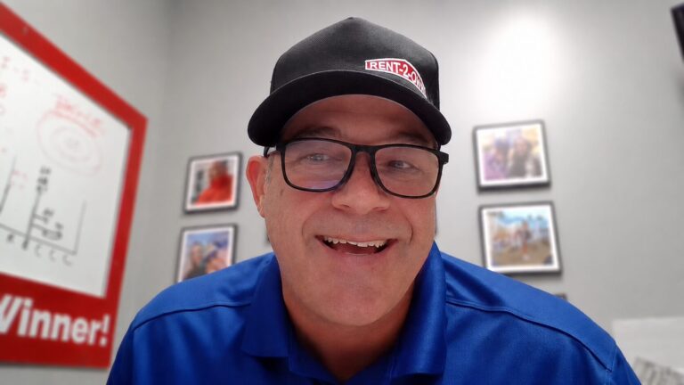 A smiling man with glasses, wearing a blue shirt and a black cap.