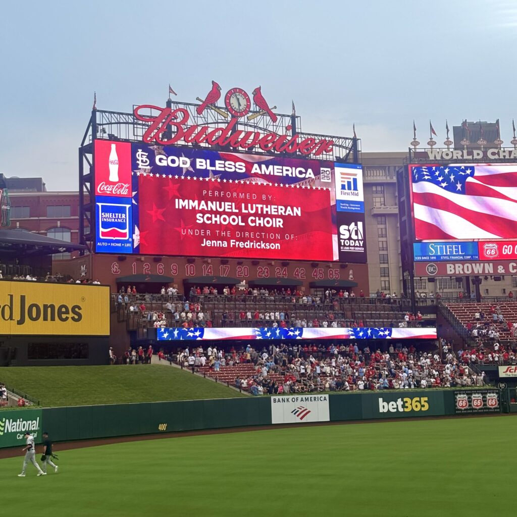 A jumbo screen at a ballpark glows brightly, topped with two large lighted cardinals and a big lighted Budweiser logo.
