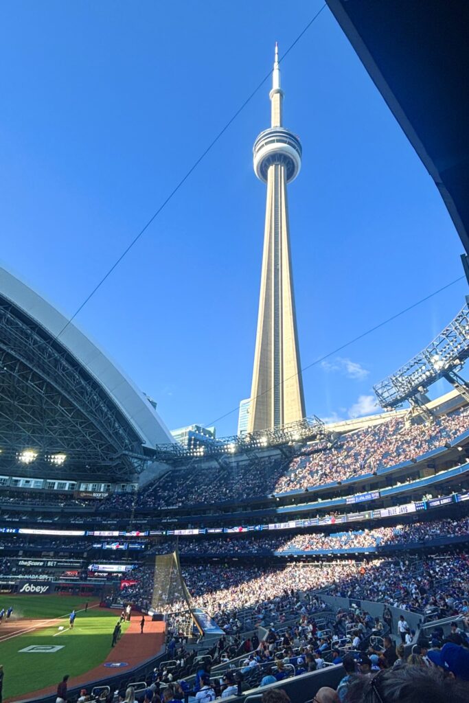 View from one side of a crowded ballpark, looking up at a huge, slim needle-like building towering above.
