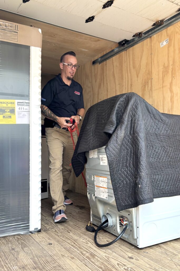A man wearing a dark Arona Home Essentials buttoned shirt and khaki pants makes his way in a crowded delivery truck toward the truck’s open back.