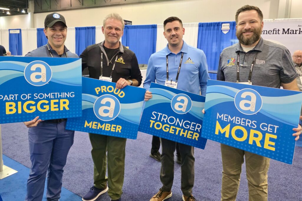 Four men holding blue APRO signs stand together smiling.