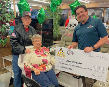 A man presents a large prize check to an elderly couple inside a showroom filled with furniture and holiday decorations.