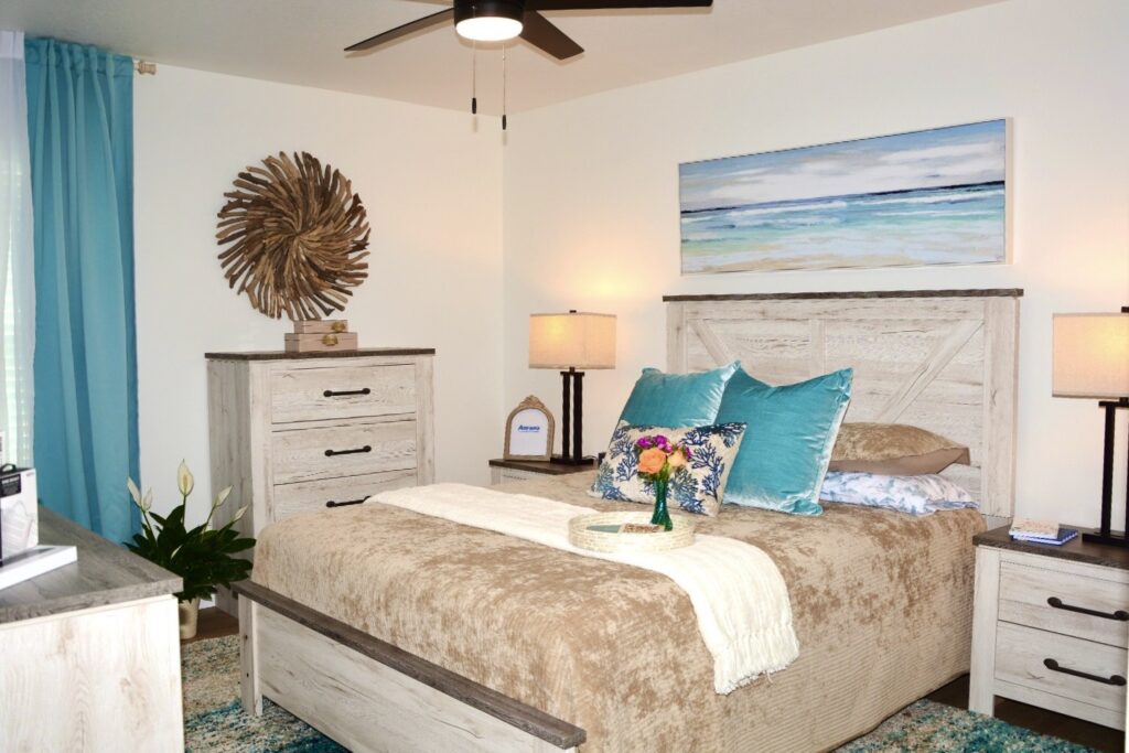 A bedroom is decorated in sand and turquoise colors, including velvety bedding, ocean and driftwood art, and a matching bedroom set of furniture.