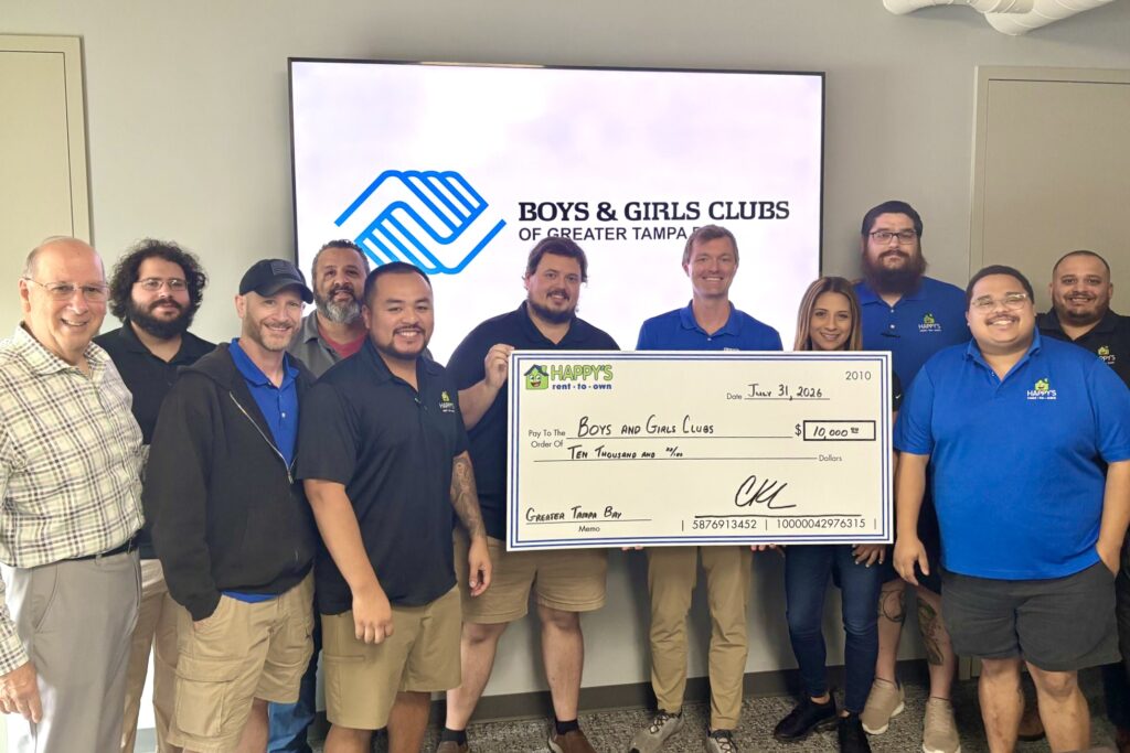 A group of people, several wearing bright blue Happy’s Home Centers logoed shirts, stand together smiling as a few hold a giant check. The check is for $10,000 to Boys & Girls Clubs of Greater Tampa Bay from Happy’s Rent-to-Own.