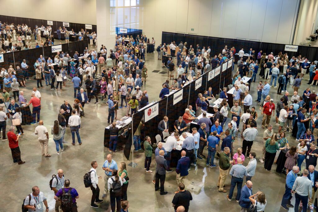 A stream of people walk along a blue carpet smiling as others applaud and high-five them from the sides.