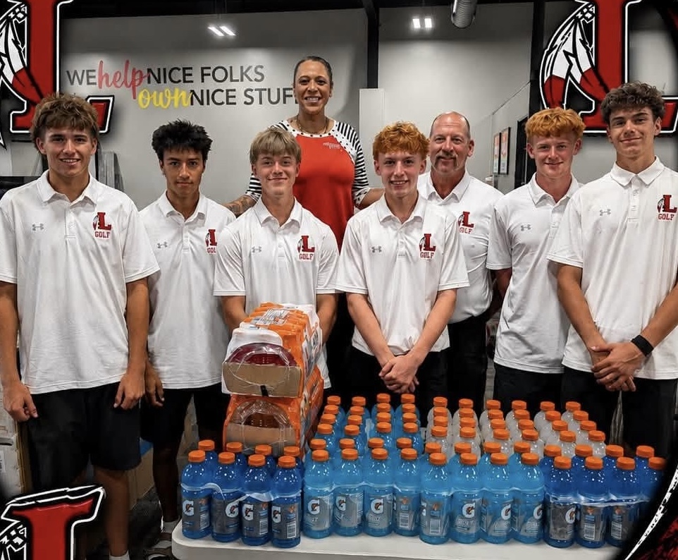 Several young men, an older man, and a woman stand smiling behind a table full of Gatorade bottles and other items. The men are wearing matching white polo shirts with London High School logos, and the photo has a London Raiders-themed frame around it.