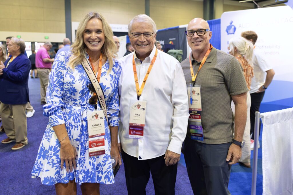 Three people – a woman, an older man, and a younger man – stand together smiling.