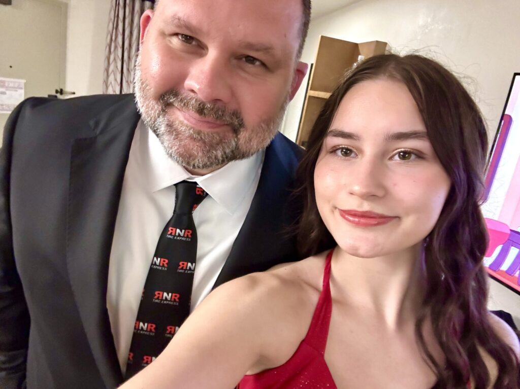 A bearded man and a young brunette woman smile for a closeup selfie.